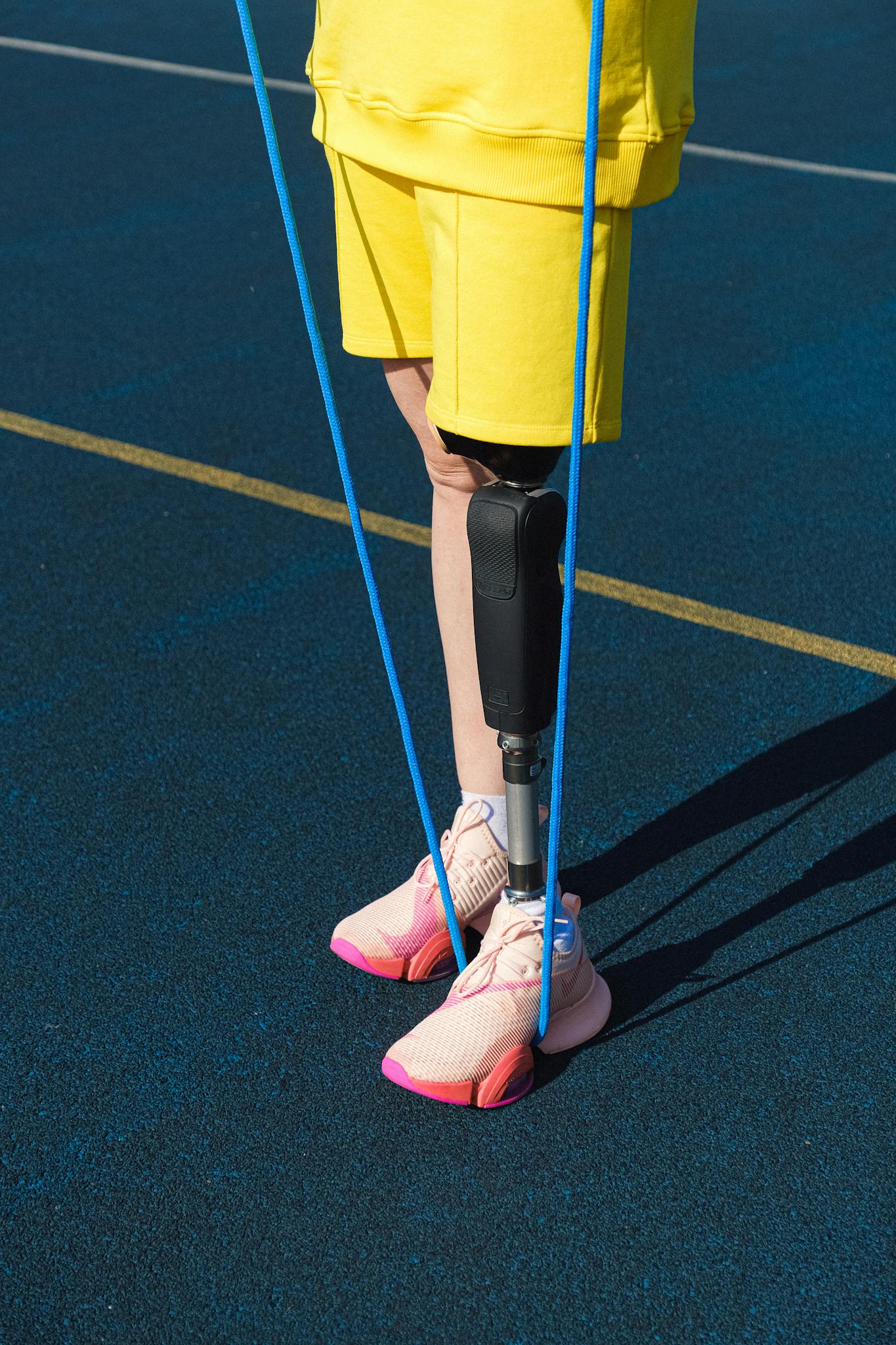 A person with a prosthetic leg skipping rope outdoors in athletic shoes and yellow clothes.