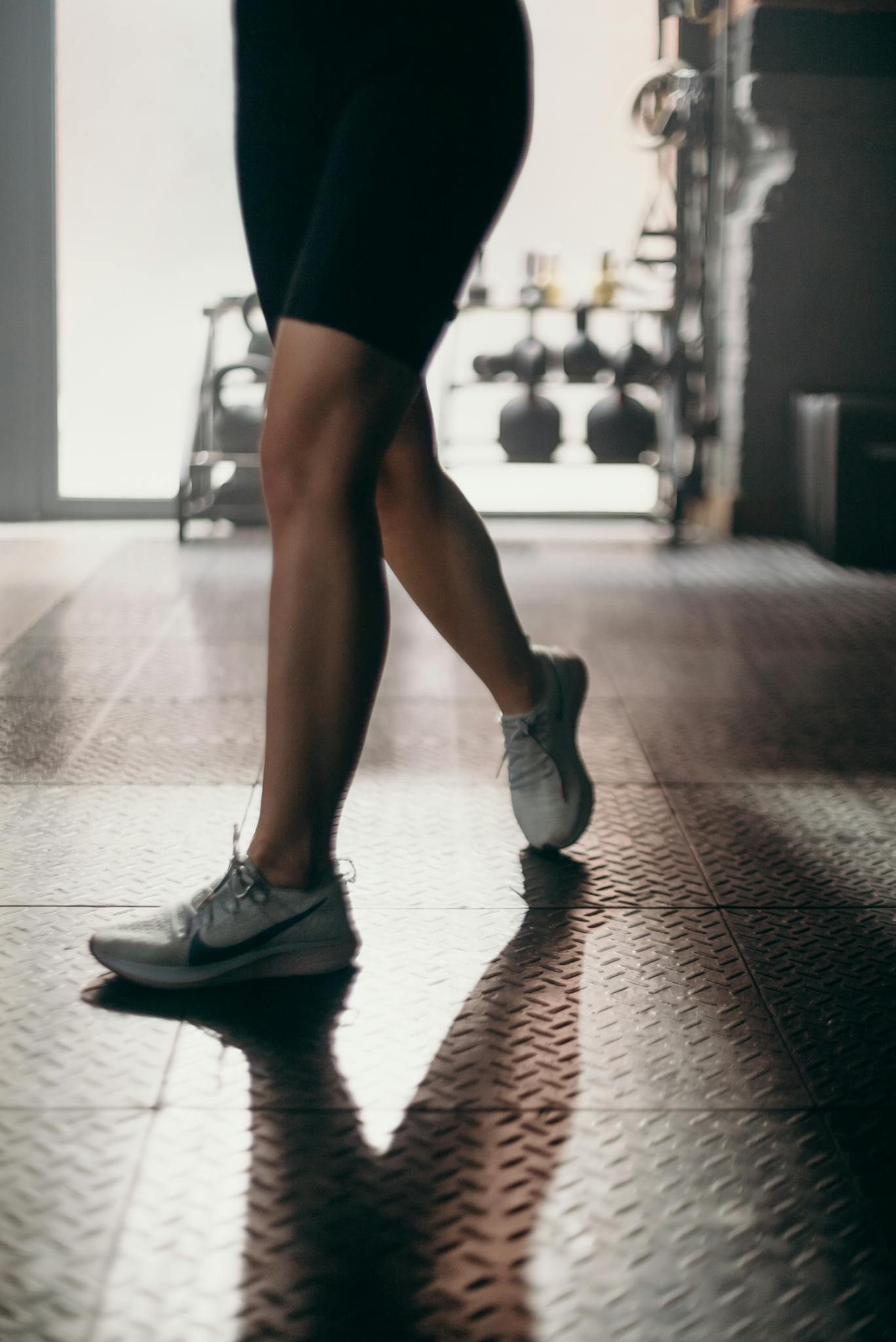Close-up of a fit woman's legs in white sneakers, walking in a gym.