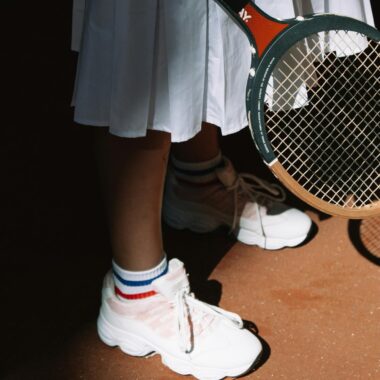 Close-up of a tennis player holding a racket, showcasing stylish sportswear and footwear.
