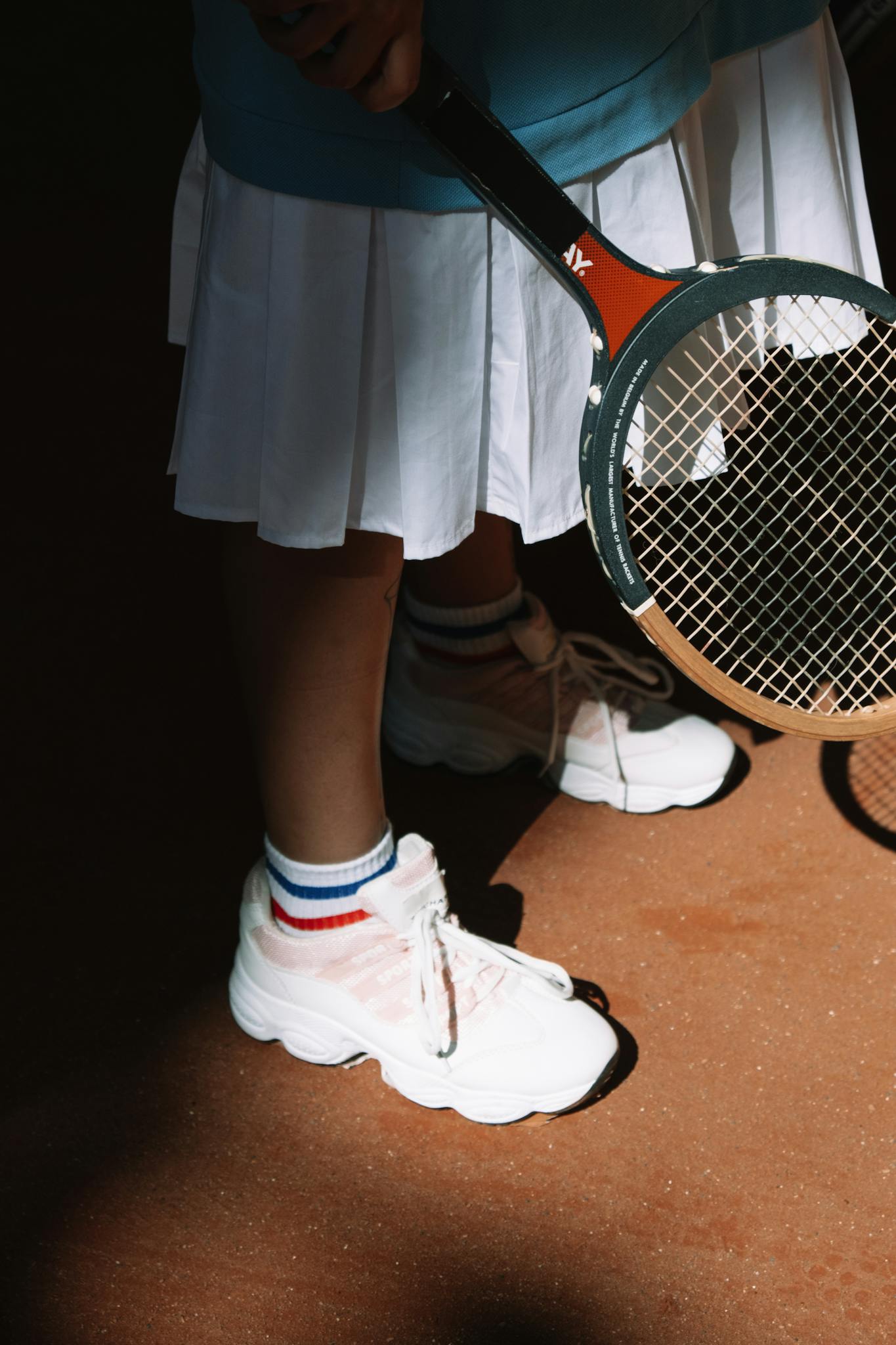 Close-up of a tennis player holding a racket, showcasing stylish sportswear and footwear.