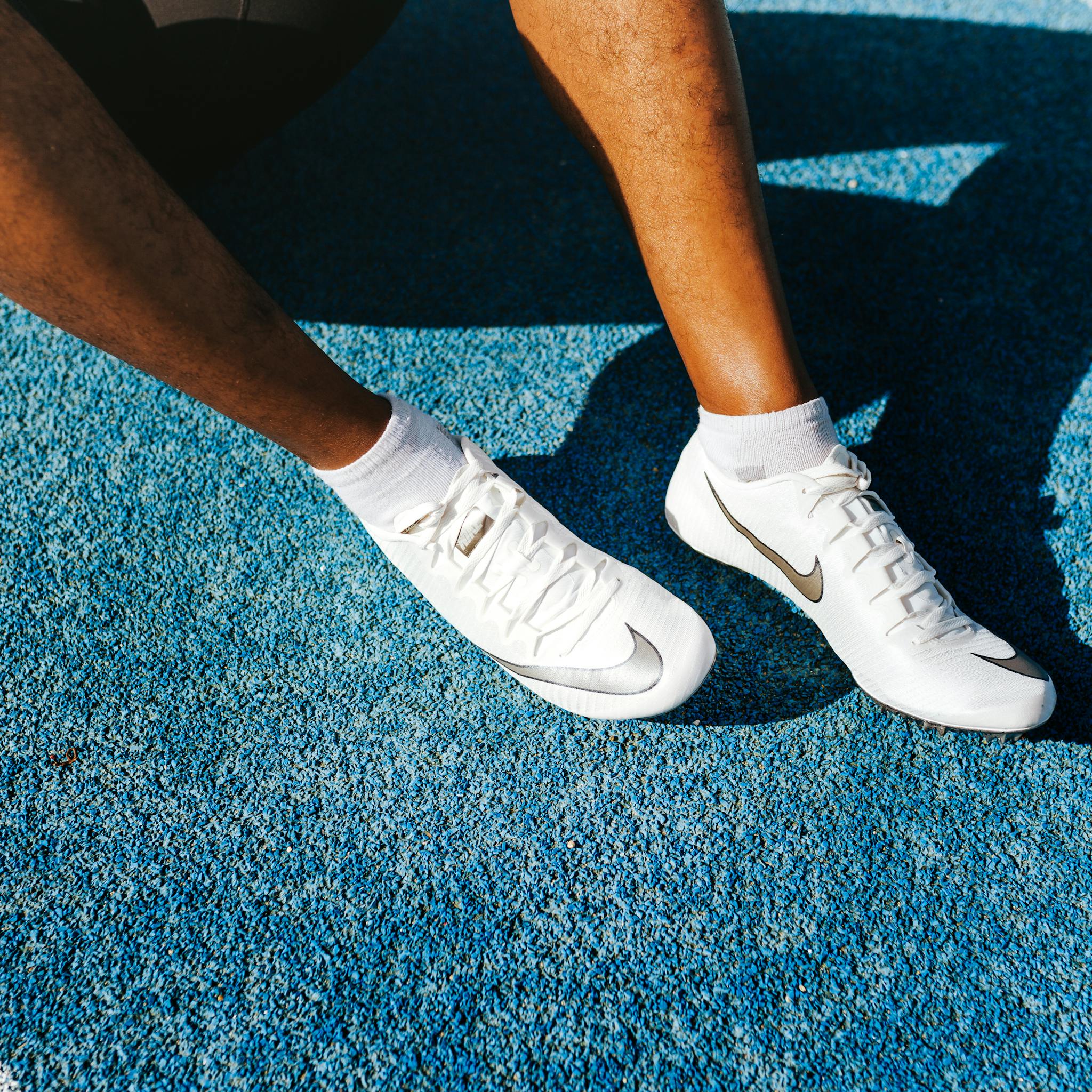 Close-up of an athlete's legs wearing Nike soccer cleats on a vibrant blue surface.
