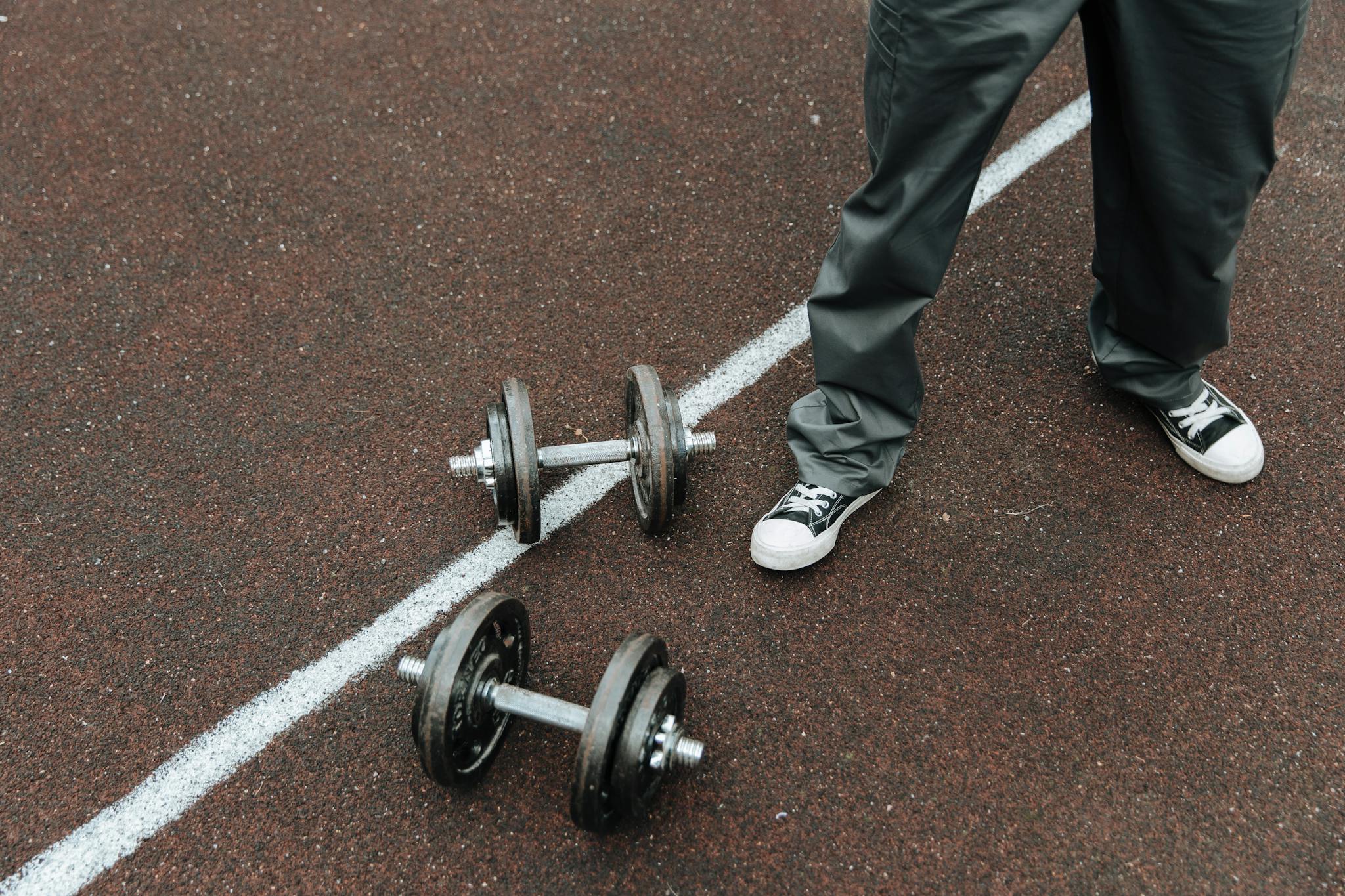 Dumbbells on an outdoor sports track with a person in casual wear.