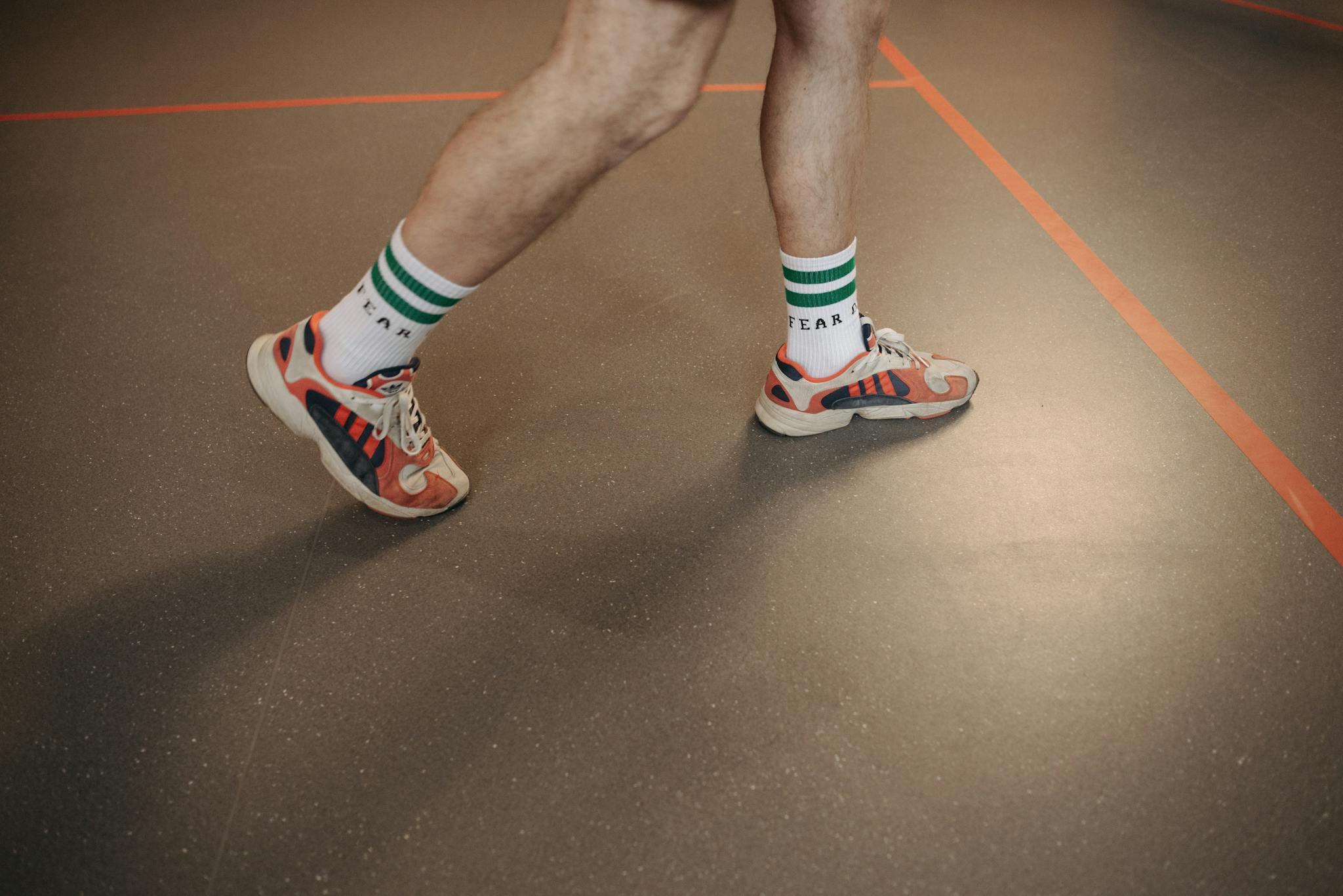 Person wearing colorful sneakers and striped socks walking indoors on a sports court.